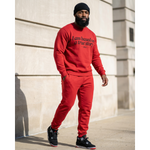 Man wearing a red sweatshirt and pants with text, standing against a light-colored wall.