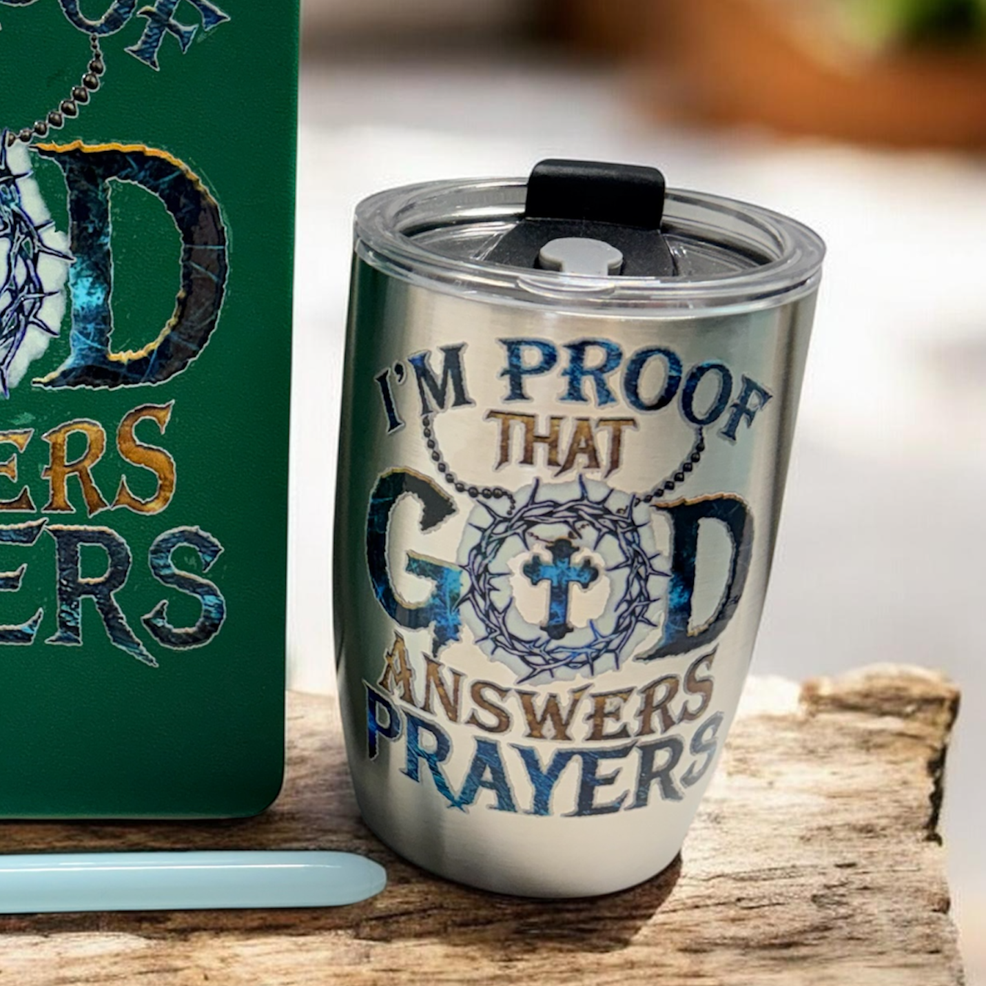 Green notebook and silver tumbler with 'I'm proof that God answers prayers' text on a wooden surface.