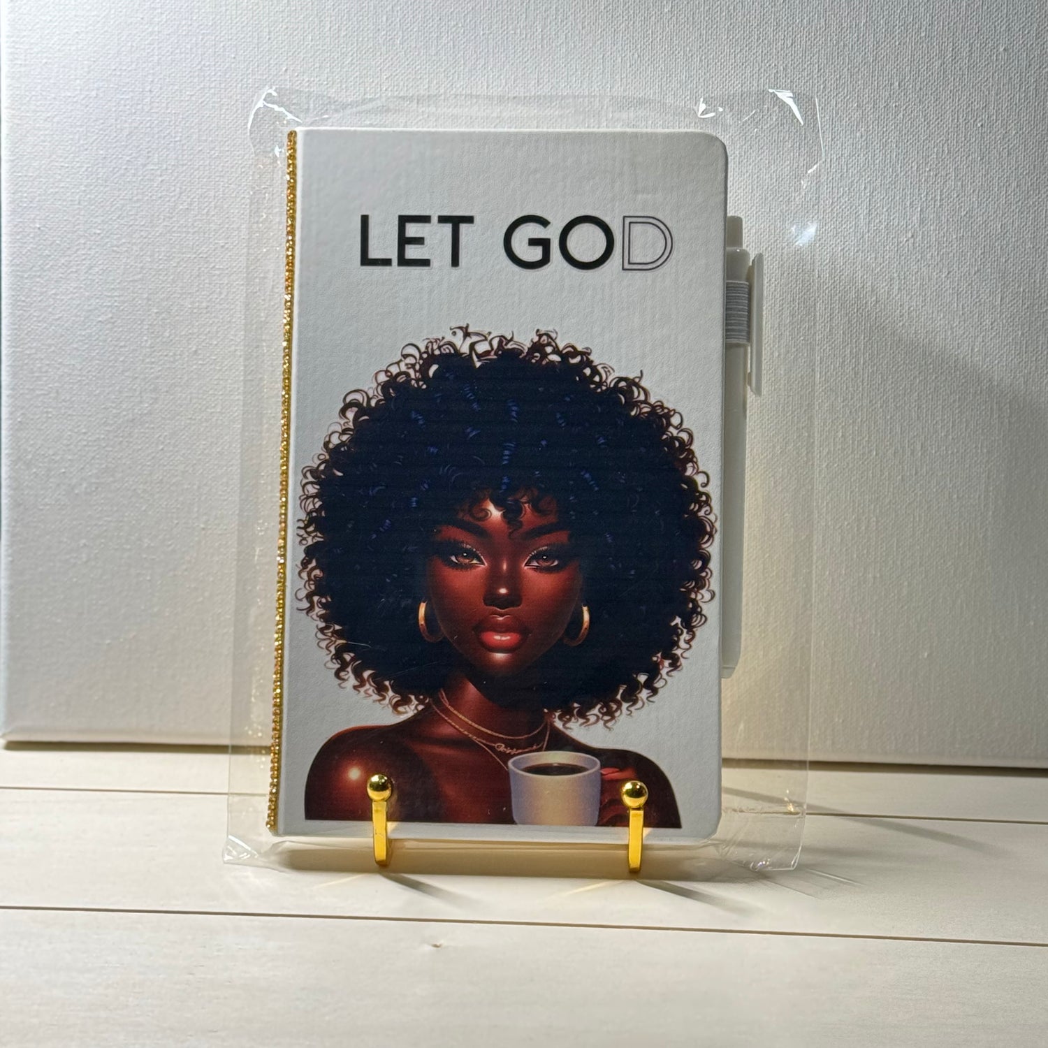 Notebook with an illustration of a woman with an afro and the text 'LET GOD' on a white background.