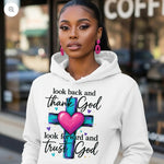 Woman wearing a white hoodie with a motivational quote and cross design, standing in front of a coffee shop.
