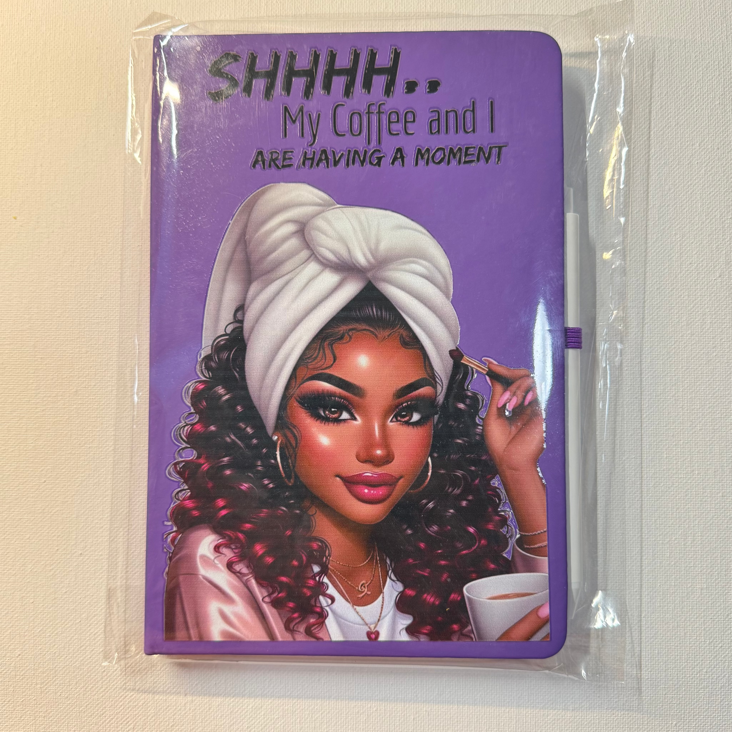 Notebook with a purple cover featuring a woman with a white turban and a coffee cup, text 'SHHHH.