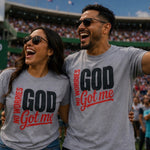 Two people wearing gray T-shirts with the printed slogan 'NO WORRIES GOD Got me' in black and red, standing in a crowded stadium. The shirt on the right also shows the Thrive Thrift Apparel logo in the upper left corner.