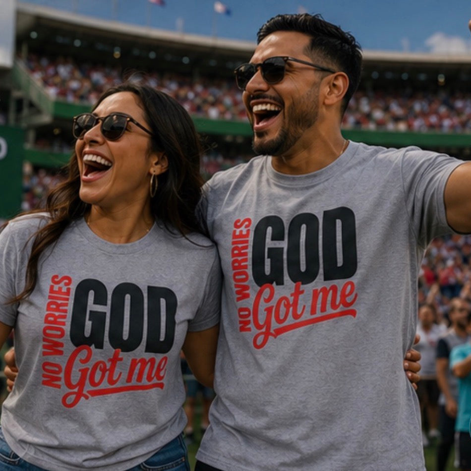 Two people wearing gray T-shirts with the printed slogan 'NO WORRIES GOD Got me' in black and red, standing in a crowded stadium. The shirt on the right also shows the Thrive Thrift Apparel logo in the upper left corner.