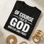 Black t-shirt with 'Of course I talk to God who else can I trust' text on a marble surface with gold chain and rings.