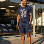 Man wearing a navy t-shirt with text standing in front of a store named 'Thrive T-Shirt Apparel Shop'.
