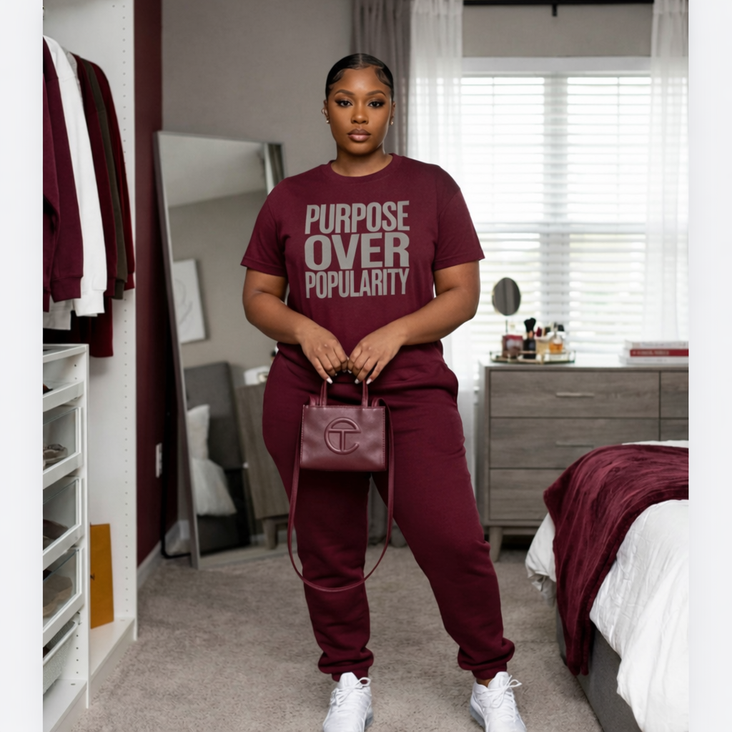 Person wearing a maroon outfit with 'Purpose Over Popularity' t-shirt in a bedroom.