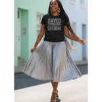 Woman wearing a black t-shirt with text and a pleated skirt outdoors.