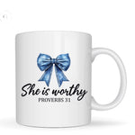 White mug with blue bow and text 'She is worthy Proverbs 31' on a white background