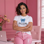 Woman wearing a white t-shirt with a blue bow and text, sitting at a desk with a laptop in a pink room.