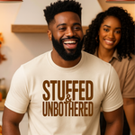 Man wearing a 'Stuffed & Unbothered' t-shirt in a kitchen setting with a woman behind him.