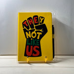 Yellow notebook with a black fist graphic and text on a white surface