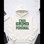 White hoodie with 'This Grind is Personal' text on a light gray surface with office items.
