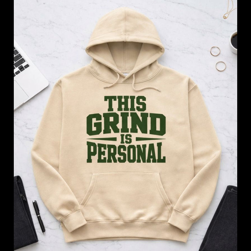 Beige hoodie with 'This Grind is Personal' text on a light gray surface.