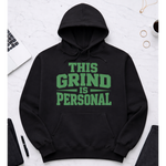 Black hoodie with 'This Grind is Personal' text on a white surface with office items.