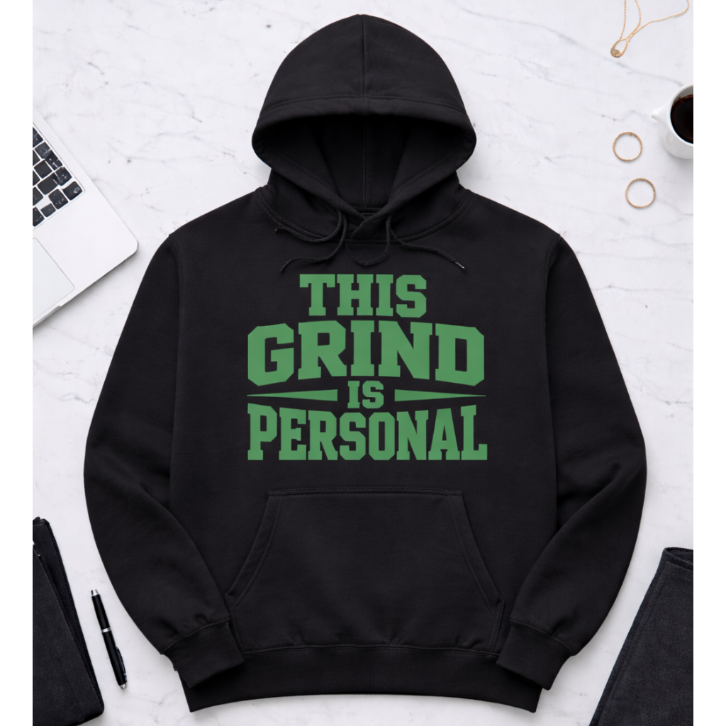 Black hoodie with 'This Grind is Personal' text on a white surface with office items.