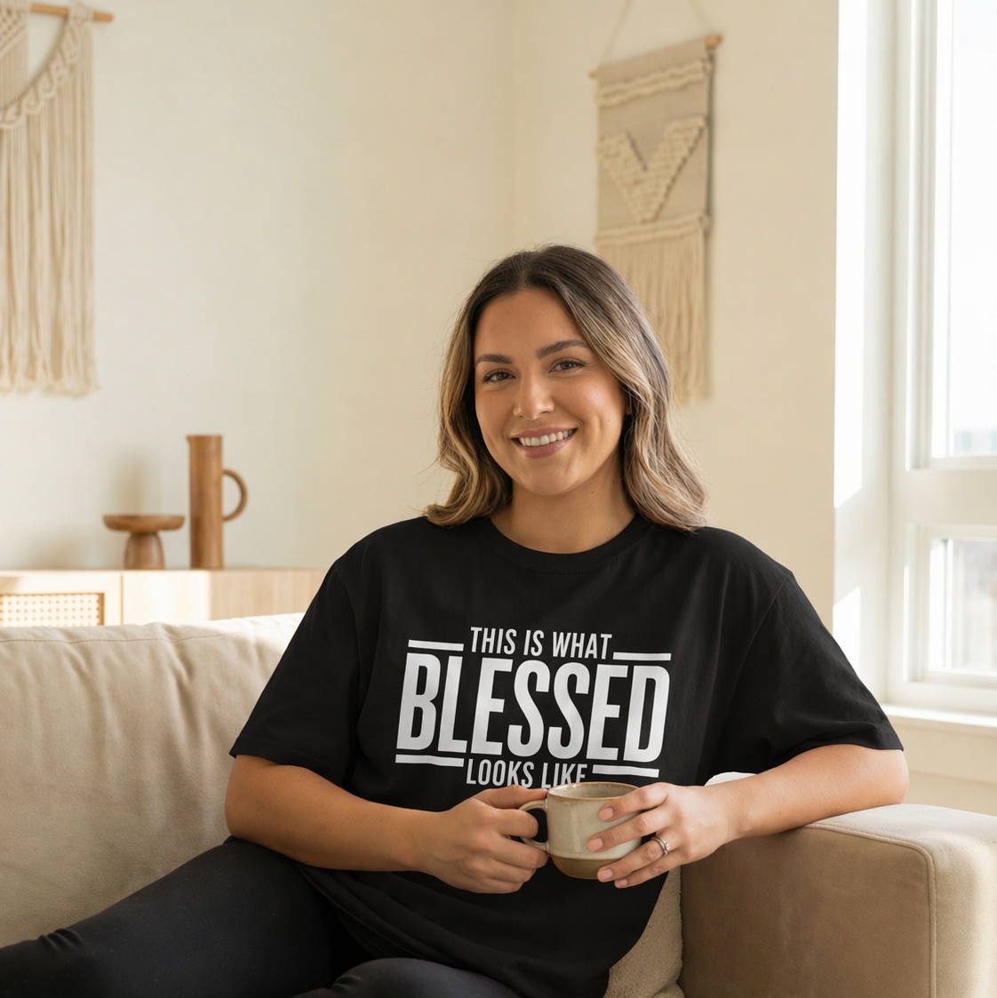 Woman sitting on a couch wearing a black t-shirt with text, holding a mug.