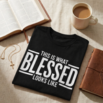 Black t-shirt with 'This is what blessed looks like' text on a table with an open book and coffee cup.