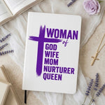 A white hardcover journal with purple text reading 'WOMAN of GOD WIFE MOM NURTERER QUEEN' and a large purple cross, styled on a beige fabric surface with lavender sprigs, an open book, a pink rose, and a gold cross necklace.