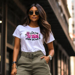 Woman wearing a white t-shirt with graphic design "YOU ARE BRAVE~STRONG~IMPORTANT~INTELLIGENT~BEAUTIFUL"  and sunglasses, standing in an urban setting.