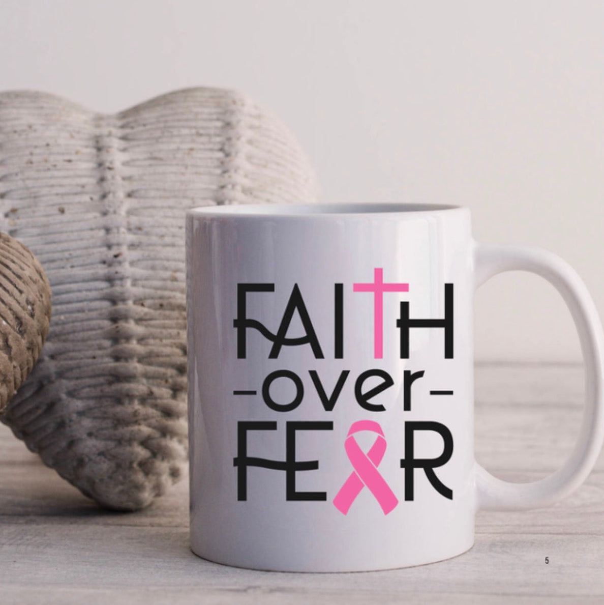 White mug with 'Faith over Fear' text and pink ribbon design on a light background