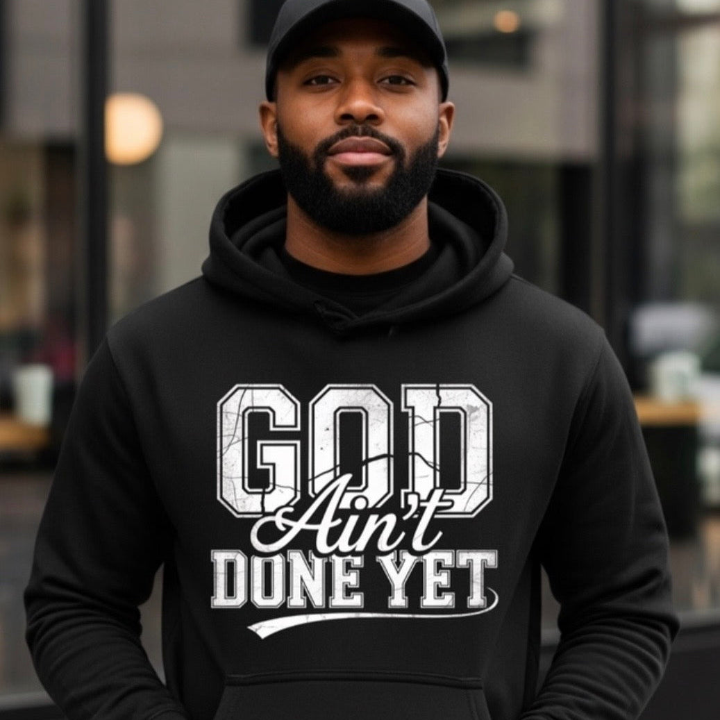 Man wearing a black hoodie with 'God Ain't Done Yet' text, standing outdoors.
