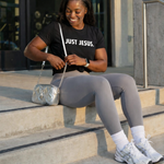 Woman sitting on steps wearing a 'Just Jesus' t-shirt in an urban setting.