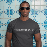 Man wearing a 'Kingdom Man' t-shirt against a blue tiled wall.