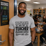 A smiling man wearing a light gray graphic T-shirt stands in a science classroom. The shirt features a black and white print with the word 'TEACHER' and small icons above it.