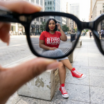 Person wearing glasses looking at a woman sitting on a bench with 'BLESSED' shirt.